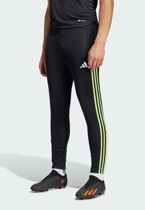 Zwarte sportleggingen met drie groene verticale strepen langs de zijkant, met een Adidas-logo. Draag het met zwarte voetbalschoenen en witte sokken.