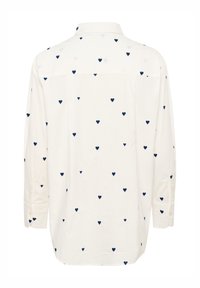 White shirt with navy heart prints, long sleeves, and a button-down collar. Made of soft fabric with a relaxed fit.