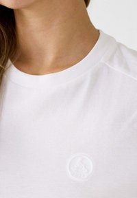 Camiseta de algodón blanca con cuello redondo y un logotipo sutil texturizado en el pecho. Tejido suave con un corte clásico.