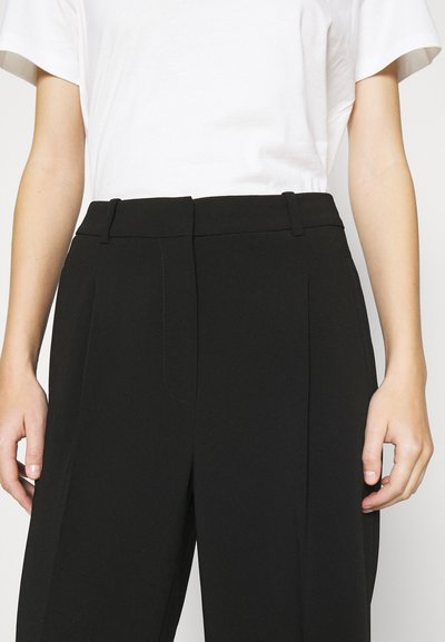 Zwarte, op maat gemaakte broek met een strak ontwerp, voorzien van een hoge taille, zijzakken en een soepele textuur. Gecombineerd met een effen wit T-shirt.