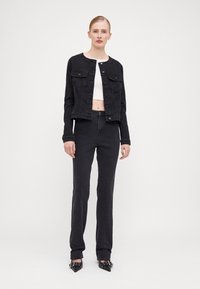 Black denim jacket with a round neckline, button closure, and two chest pockets, paired with matching black denim pants and pointed toe shoes.