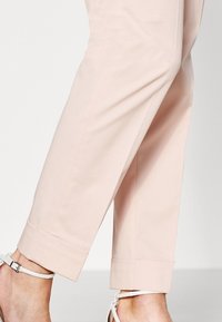 Pantalons tapered rose pâle avec ourlet retroussé, en tissu lisse, dotés de poches latérales et d'une coupe ajustée.