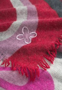 Rood en roze gebreide sjaal met franjes, voorzien van een subtiele geborduurde bloemdetail op een zachte, gestructureerde achtergrond.