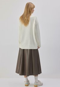 Pull crème surdimensionné avec ourlet côtelé, associé à une jupe plissée marron foncé. Le modèle porte des baskets blanches et des chaussettes blanches.