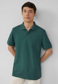 Grüne Poloshirt mit Kragen, einer Vorderpartie mit zwei Knöpfen, kurzen Ärmeln und einem entspannten Schnitt. Glattes Baumwollgewebe.
