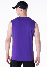 Αμάνικο αθλητικό μπλουζάκι σε μοβ χρώμα με κίτρινες πλευρικές λεπτομέρειες. Κατασκευασμένο από μαλακό ύφασμα με άνετη εφαρμογή. Μαύρο καπέλο με καμπύλη γείσο.