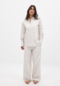 Striped pajama set in light beige and white, features a button-up collared shirt with long sleeves and loose, wide-leg pants. Smooth texture.