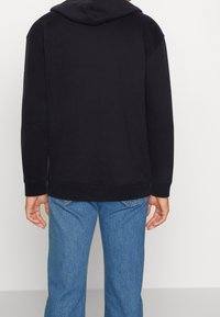 Svart hoodie med avslappnad passform, med ribbade mudd och nederkant, kombinerad med ljusblå jeans. Enkelt design, utan mönster.