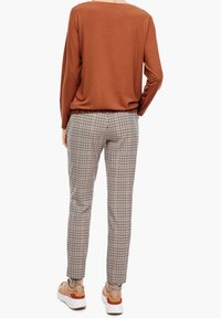 Rdzawy, długi rękaw z szerokim dekoltem. Spodnie w kratę w kolorze beżowym, czarnym i różowym mają slim fit. Obuwie jest lekkie z akcentami.