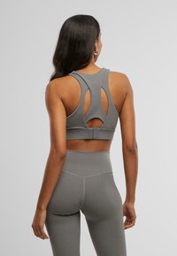 Grijze sportbh met een uitgesneden achterkant, voorzien van een gladde textuur en dikke bandjes. Gepaard met hooggewaist grijze leggings.
