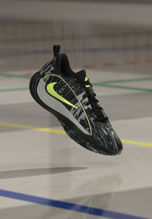 Sort og grå marmor sportssko med sorte snørebånd og neon-gult swoosh-logo svævende over et poleret indendørs banegulv.