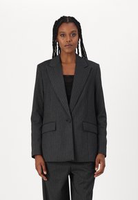 Tumehall pinstripe bleiser, millel on üks nööp ja nokalapid, ning esi-taskud. Kanda musta pluusi peal, sile tekstuur.
