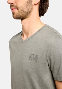 Sivé tričko s výstrihom do V vyrobené z jemnej bavlny. Na hrudi má jemne vyrazené logo. Klasický strih s krátkymi rukávmi a hladkou textúrou.