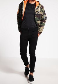 Kamelotová bomber bunda s oranžovou podšívkou, černé tričko s potiskem, černé slim džíny a černé nazouvací boty.