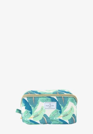 Une trousse de toilette rectangulaire zippée, ornée d’un motif de feuilles bleu, vert et blanc, avec une étiquette sur le devant portant l’inscription « The Flat Lay Co. London. »