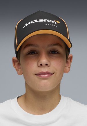 Young person wearing a black and orange McLaren Racing cap and a white shirt, facing forward with a neutral expression.