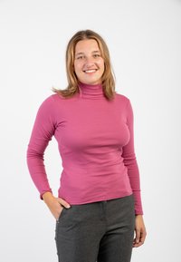 Maglietta a maniche lunghe aderente con collo alto di colore rosa chiaro, realizzata in tessuto morbido, abbinata a pantaloni grigi su misura. Texture liscia, design minimalista.