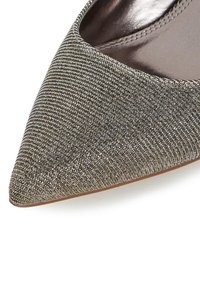 Zapato de punta afilada con un tejido metálico plateado-gris, texturizado y con un brillo sutil, y un forro interior suave.