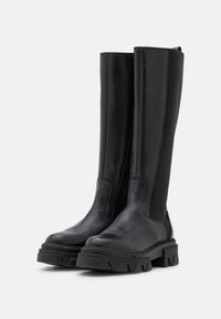 Botas negras hasta la rodilla con cuero liso y paneles laterales elásticos, con una suela de goma gruesa y puntera reforzada para mayor durabilidad.