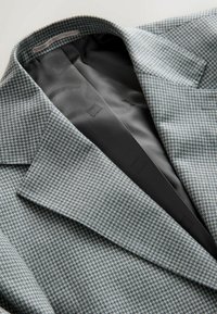 Gray houndstooth patterned blazer with a black lining, featuring notched lapels and a sharp, tailored silhouette.