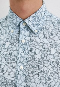 Camicia di jeans azzurro chiaro con un motivo floreale nero, colletto alla francese e bottoni bianchi, realizzata in tessuto testurizzato.