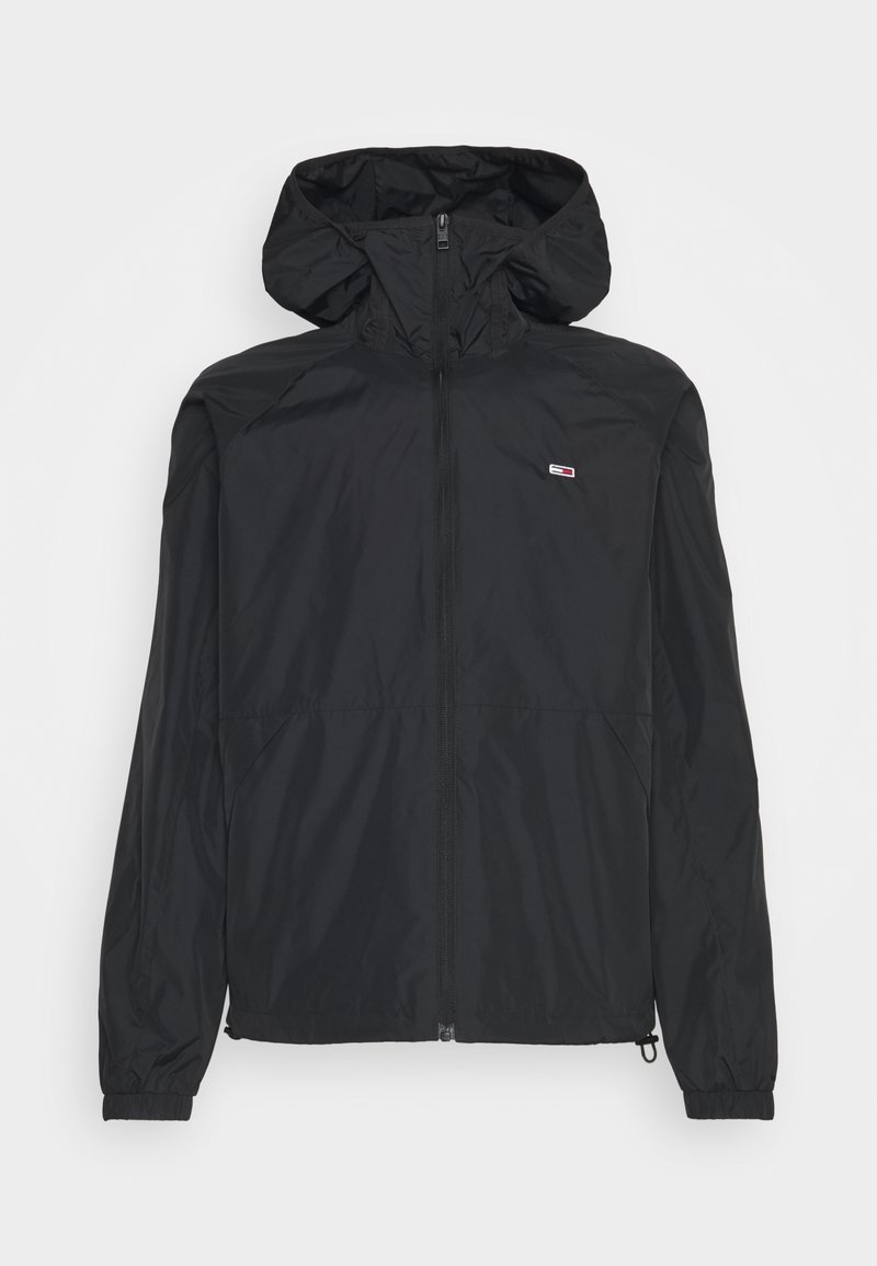 Wodoodporna czarna kurtka z kapturem, przednim zamkiem błyskawicznym, elastycznymi mankietami oraz małą naszywką z logo na piersi. Gładka faktura i lekka konstrukcja.