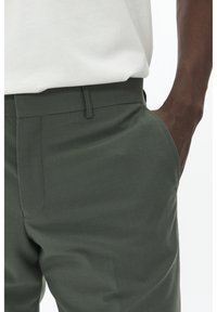 Pantalons verts texturés avec une coupe droite et des poches latérales. Dotés d'une taille plate, d'un tissu lisse et de détails de couture subtils.