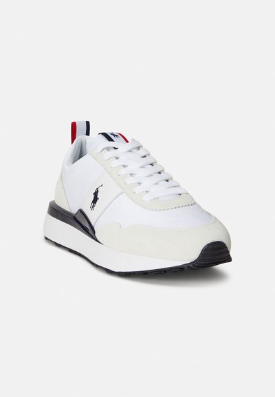 Fehér tornacipő hálós és hasított bőr anyagból, fekete talppal, hímzett logóval, valamint piros és tengerészkék díszítéssel a saroknál és a nyelvnél.