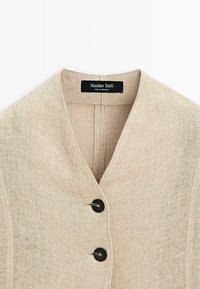 Beige linned blazer med V-hals, der har to mørke knapper og en subtil tekstur. Etiketten siger "Massimo Dutti, lavet i Marokko."