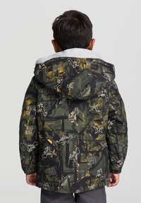 Puchowa kurtka w kolorze czarnym i zielonym z nadrukiem dinozaurów oraz szarym kapturem. Posiada elastyczne mankiety oraz sznurek w dolnej części.