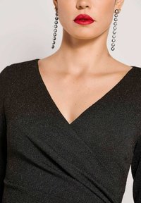 Zwart wikkeljurkje met V-hals, gemaakt van een gestructureerde, sprankelende stof. Lange mouwen en opvallende hangers accentueren de uitstraling.