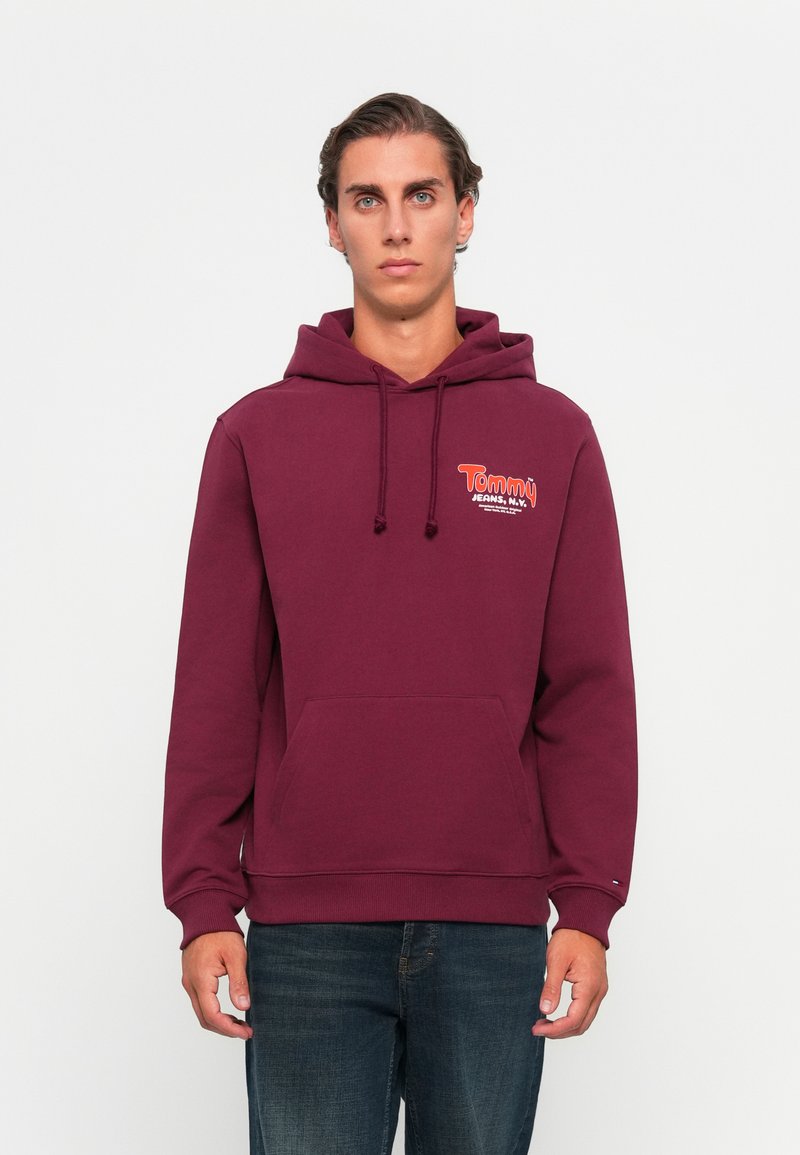 Bordeaux hættetrøje med en frontlomme, der har "Tommy Jeans" logo i kontrasterende farver på brystet. I bomuldsstof, afslappet pasform.