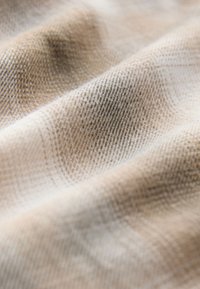 Bézs és világosbarna kockás szövet puha textúrával, finoman fénylő, keresztezett vonalakat alkotó szövött mintával.