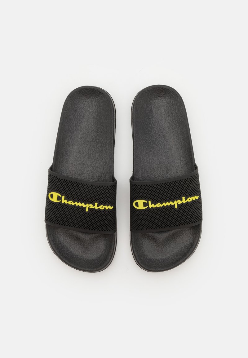 Schwarze Slide-Sandalen mit einem strukturierten Riemen, der das gelbe "Champion"-Logo zeigt. Hergestellt aus synthetischem Material, flaches Design, offene Zehen.