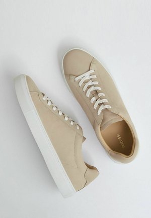 Beige ruskind sneakers med hvide gummisåler, der har flade hvide snørebånd og et minimalistisk design uden yderligere mønstre eller accenter.