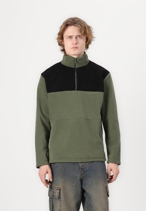 Zaļa fleece džemperis ar melniem akcentiem, augstu apkakli un ar rāvējslēdzēju. Iezīmē kontrastējošu paneļu dizainu un garām piedurknēm.