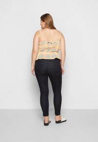 Top peplum de gingham multicolor com alças ajustáveis, combinado com jeans skinny escuros e sapatos slip-on de cor clara.