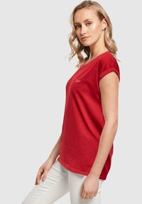 Rød kortærmet t-shirt lavet af blød bomuld. Har en rund halsudskæring og opfoldede manchetter. Diskret logo detaljeret på venstre bryst.