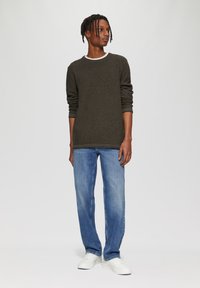 Dunkelgrünes, strukturiertes Langarmoberteil mit weißem Rundhalsausschnitt, kombiniert mit hellblauen geraden Jeans und weißen Sneakers.