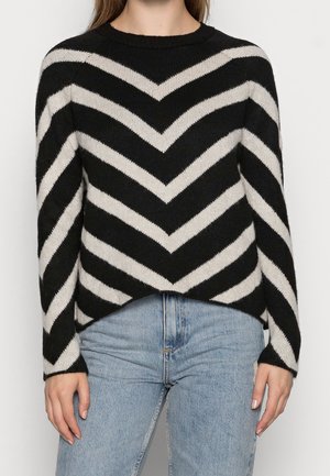 Maglione a righe a zigzag in bianco e nero, texture lavorata a maglia, collo rotondo, maniche lunghe, design corto, abbinato a jeans azzurri.
