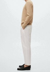 Beige gebreide trui, crèmekleurige broek en zwarte loafers. De outfit heeft een comfortabele pasvorm en gladde texturen met zichtbare zijzakken.