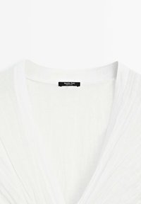 Witte linnen blouse met een diepe V-halslijn, voorzien van subtiele plooien en een zwart label met de tekst "Massimo Dutti." Zachte, lichte textuur.