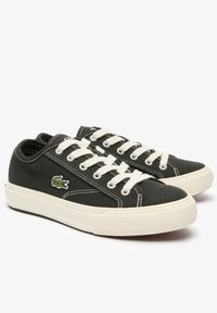 Sneaker in tela nera con design con lacci bianchi, cuciture a contrasto, suola in gomma e logo di coccodrillo ricamato verde sul lato.