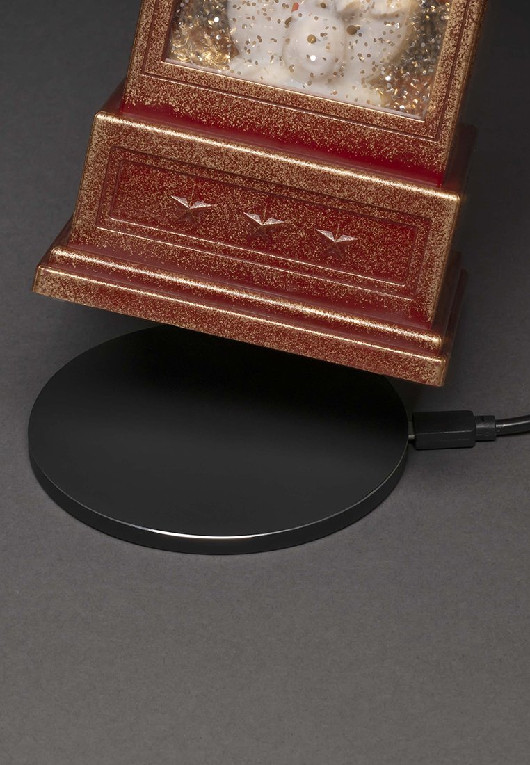 Rotierende Rot- und Gold-Schneekugel auf einem schwarzen, runden drahtlosen Ladepad mit angeschlossenem USB-Kabel.