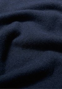 Marineblauwe stof met een zachte, gestructureerde oppervlakte, waarop een fijn breipatroon zichtbaar is. Het materiaal strålt warmte en gezelligheid uit.