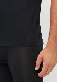 Schwarzes Sportshirt aus glattem Stoff mit einer Nahtgestaltung und kleinem Logo am Saum, kombiniert mit enganliegenden schwarzen Leggings.