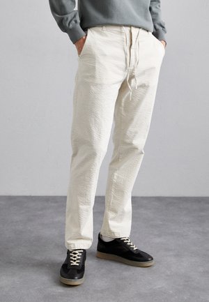 Pantalons blancs texturés avec une coupe décontractée et une taille à cordon, accompagnés de baskets noires avec des lacets crème et une semelle en gomme.