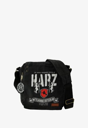 Schwarze Canvas-Umhängetasche mit einem bedruckten Design, das "HARZ" und ein rotes Wappen zeigt. Enthält einen Reißverschluss, einen Riemen und ein Logo-Tag. Abmessungen nicht angegeben.