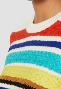 Neulepaita, jossa on vaakasuorat raidat punaisena, oranssina, keltaisena, turkoosina, sinisenä, ruskeana ja kermaisenä; teksturoitu lanka ja ribattua kaula-aukkoa.