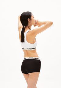 Weißer Sport-BH mit breitem schwarzem Band, das "ARMEDANGELS" beschriftet ist, und schwarzen Boyshorts mit passendem Bund, glattes Material, körpernaher Schnitt.